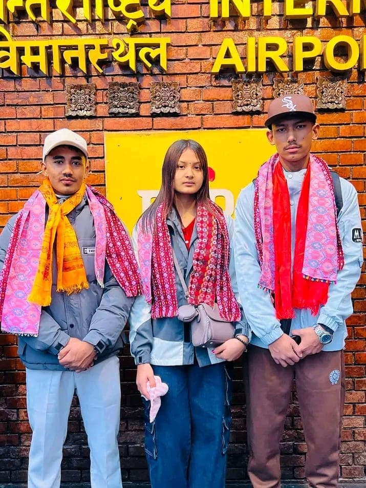 Three students wearing farewell scarves outside the international airport in Kathmandu