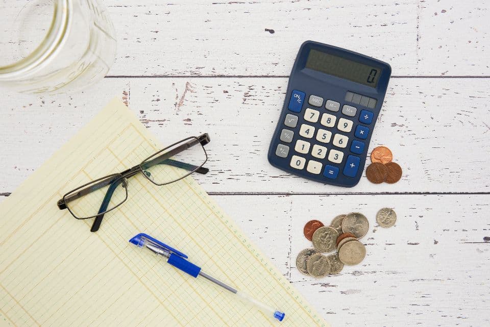 A calculator, coins, glasses and a notepad on a desk