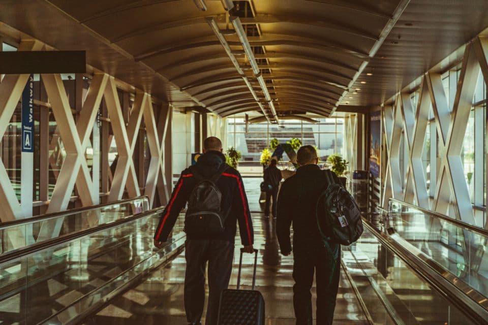 Travellers with backpacks walking through an airport terminal walkway